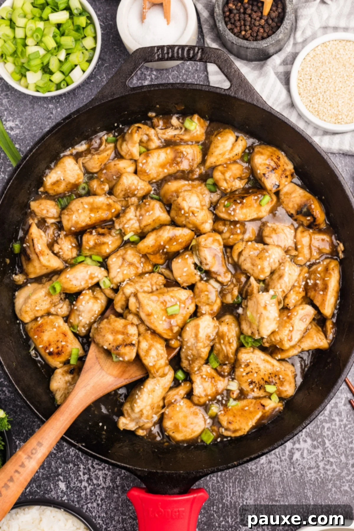 Sticky Honey Ginger Chicken 2 A cast iron skillet filled with golden honey ginger chicken stir fry, being scooped with a wooden spoon, ready to serve.