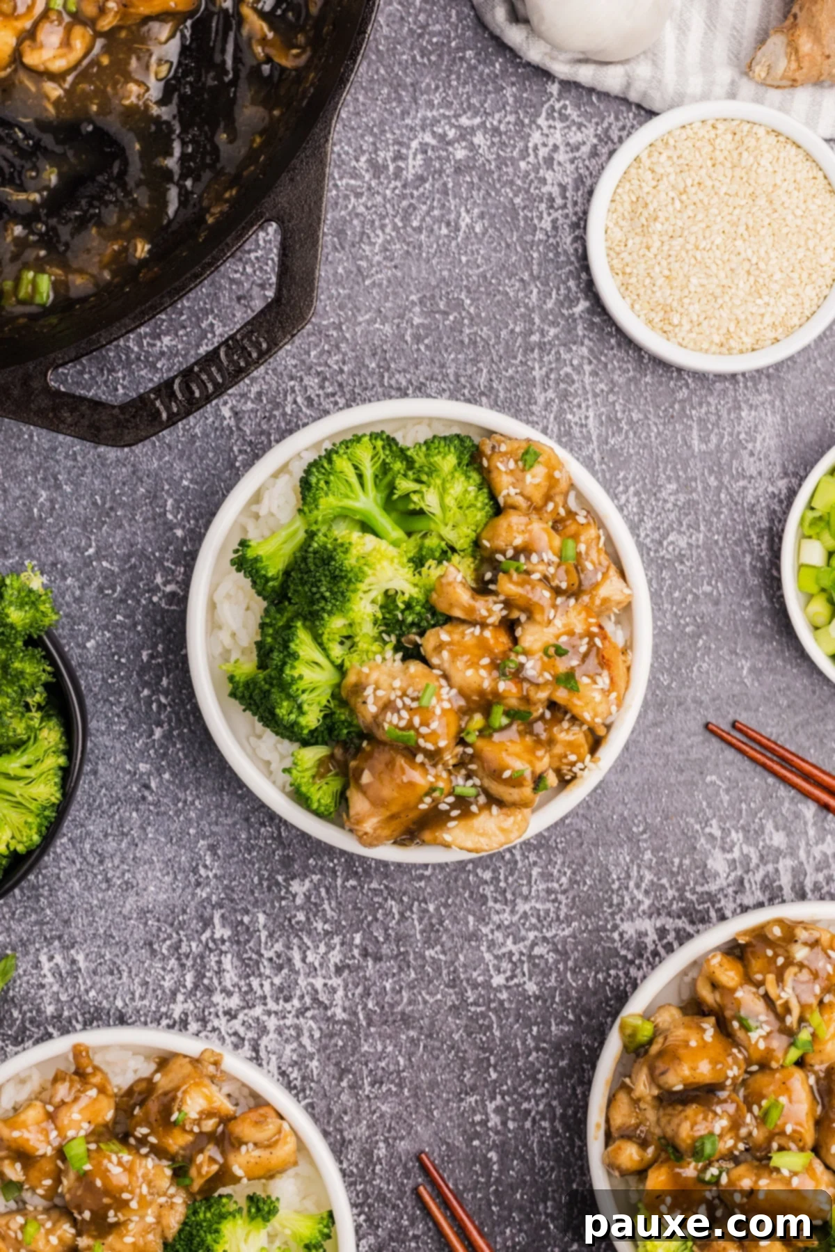 Sticky Honey Ginger Chicken 5 A beautifully presented bowl with honey ginger chicken stir fry, steamed broccoli, and cooked rice, surrounded by small condiment bowls.