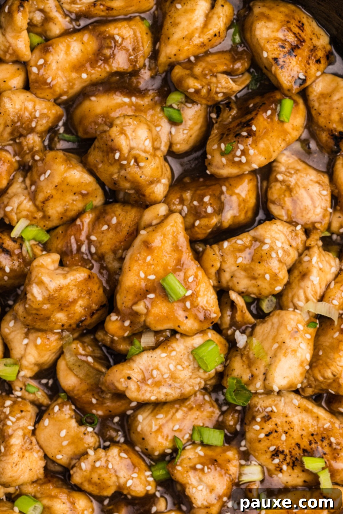 Sticky Honey Ginger Chicken 6 A close-up shot of tender, cubed chicken pieces coated in a rich, golden honey ginger sauce, glistening in a skillet.
