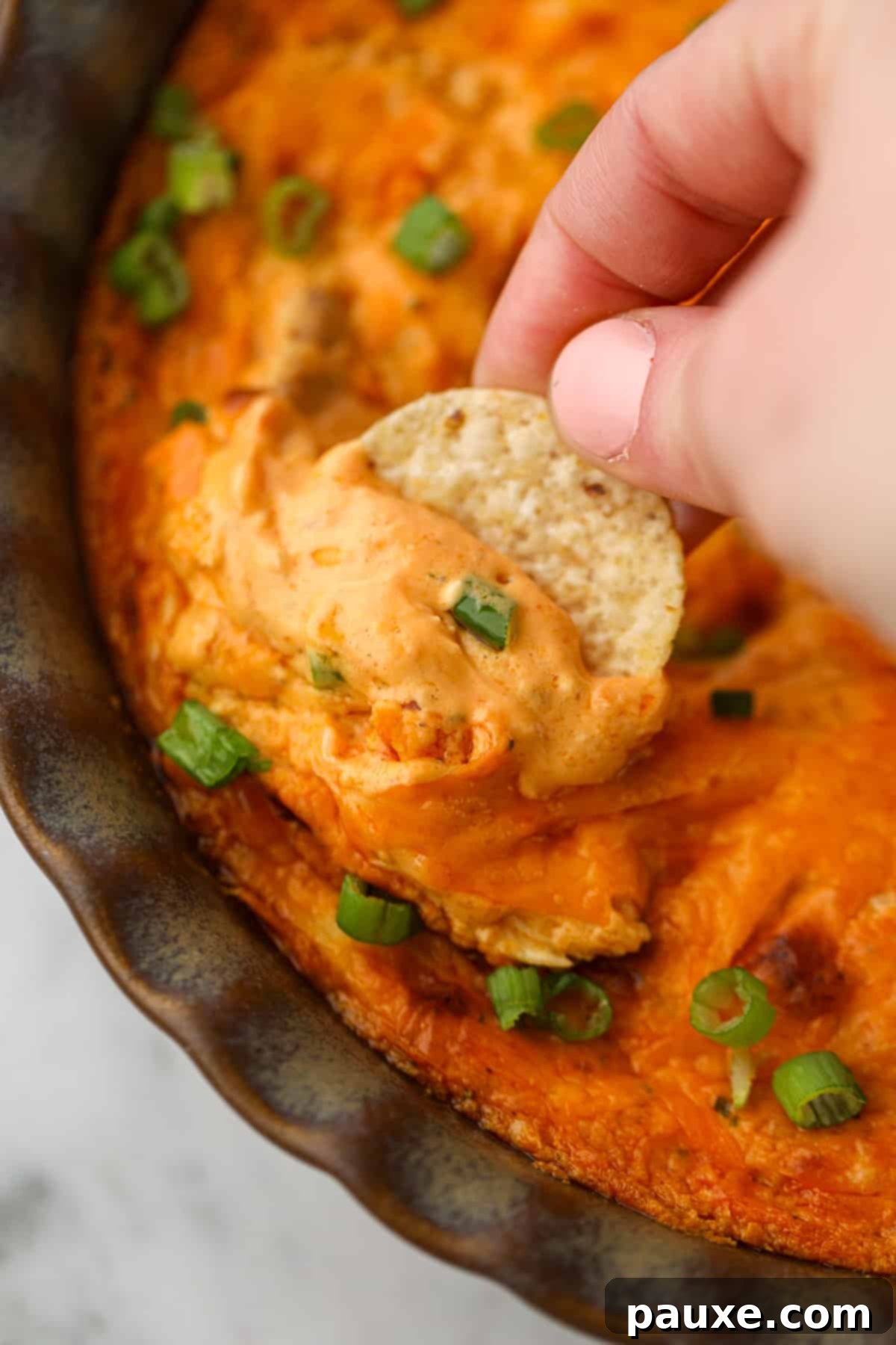 Irresistible Buffalo Chicken Dip 2 Dipping a tortilla chip into a cheesy buffalo dip, showing its creamy texture and vibrant color.