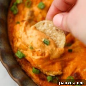 Irresistible Buffalo Chicken Dip 8 Dipping a tortilla chip into a bright orange chicken dip, highlighting its appetizing color and texture.