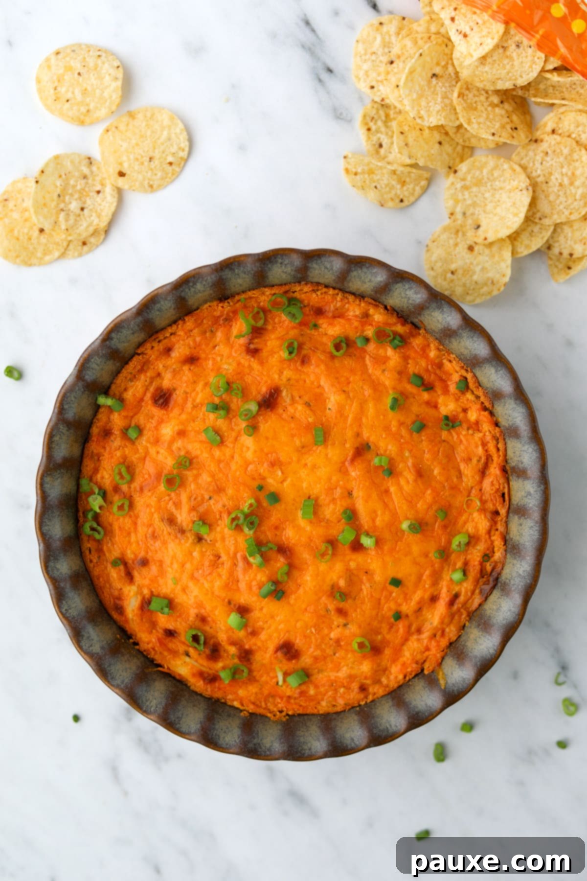 Irresistible Buffalo Chicken Dip 5 A brightly colored, freshly baked buffalo chicken dip in a pie plate, surrounded by an array of crunchy tortilla chips, ready for serving.