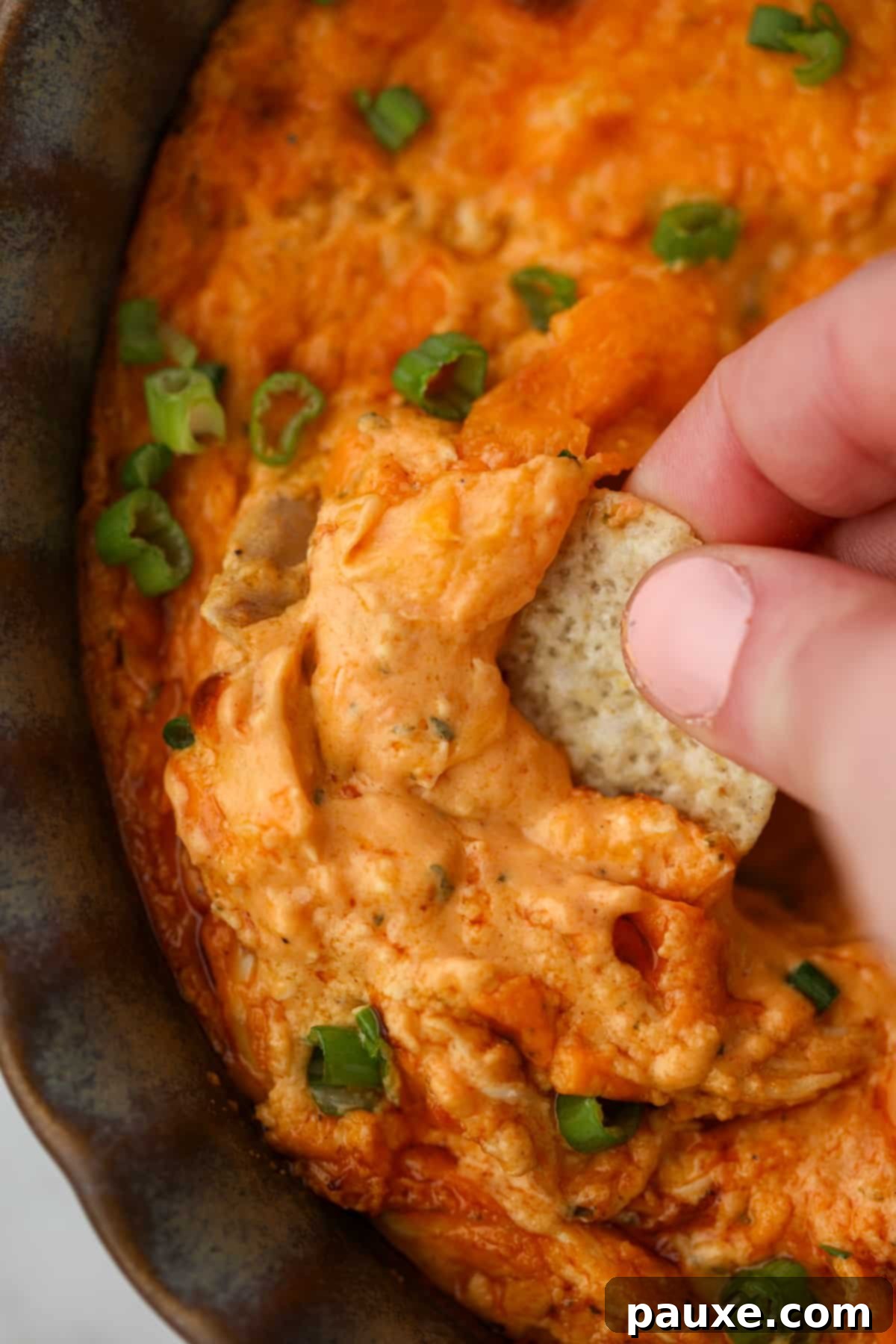 Irresistible Buffalo Chicken Dip 6 A close-up shot of a tortilla chip being dipped into a brightly colored, hot, and creamy buffalo chicken dip, highlighting its inviting texture.