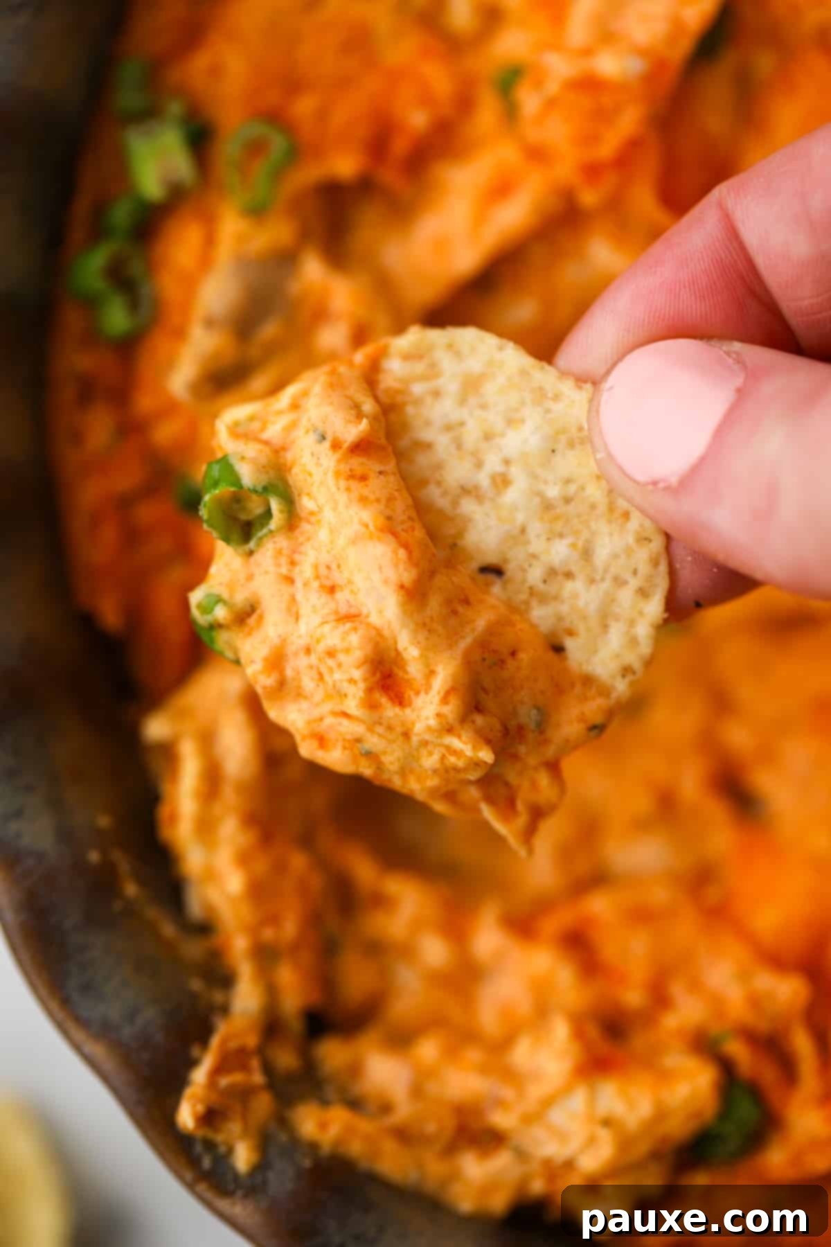 Irresistible Buffalo Chicken Dip 7 A close-up of a bubbling, hot Buffalo Chicken Dip in a baking dish, with a tortilla chip poised to dip, emphasizing its readiness to be enjoyed.