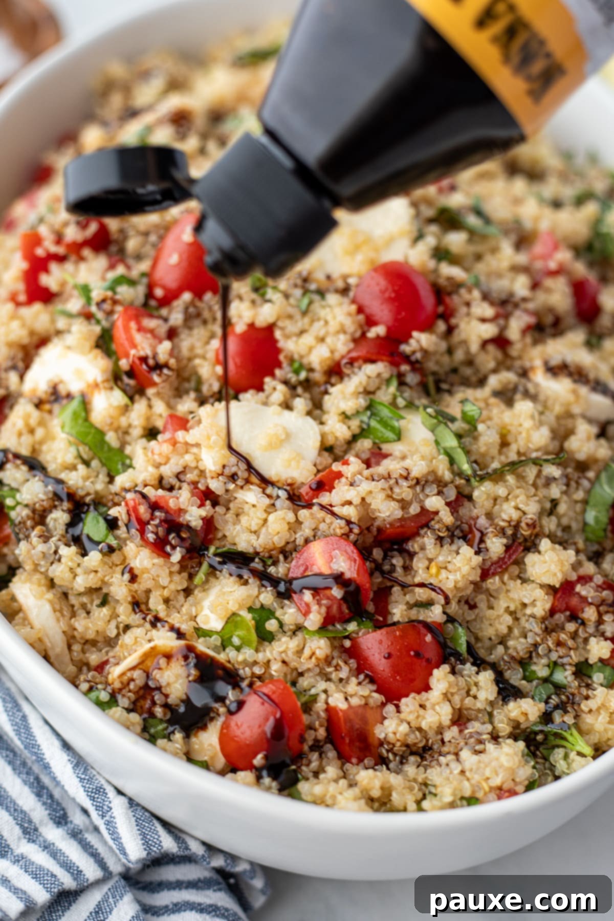 Vibrant Quinoa Caprese 5 Balsamic glaze being drizzled on top of a quinoa salad in a large serving bowl.