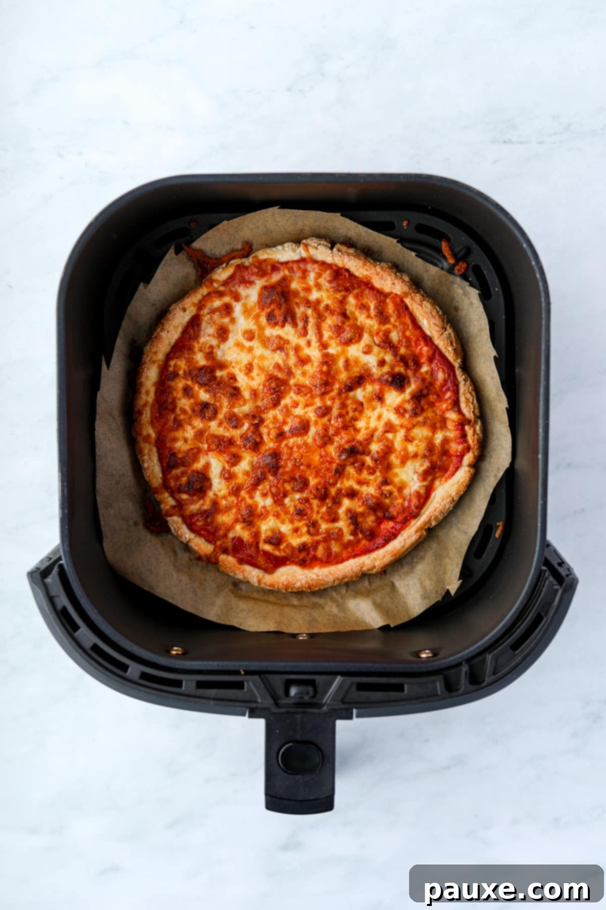 Wholesome Yogurt Pizza 9 An air fryer with a cooked cheese pizza inside, bubbling and golden.