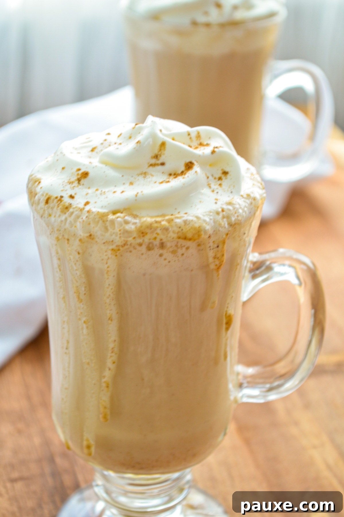 Homemade Instant Pot Pumpkin Spice Latte 2 Two glasses of homemade pumpkin spice lattes, generously topped with whipped cream and a sprinkle of autumnal spices, creating a warm and inviting scene for Fall.