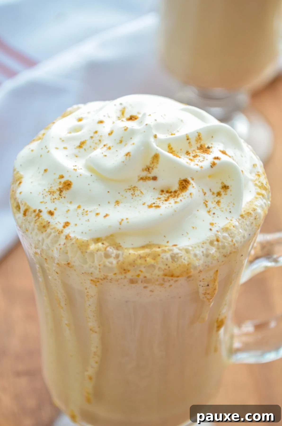 Homemade Instant Pot Pumpkin Spice Latte 5 A stunning close-up of a glass mug filled with a rich, inviting pumpkin spice latte, crowned with a tall swirl of whipped cream and a dusting of pumpkin spice, ready to be enjoyed.