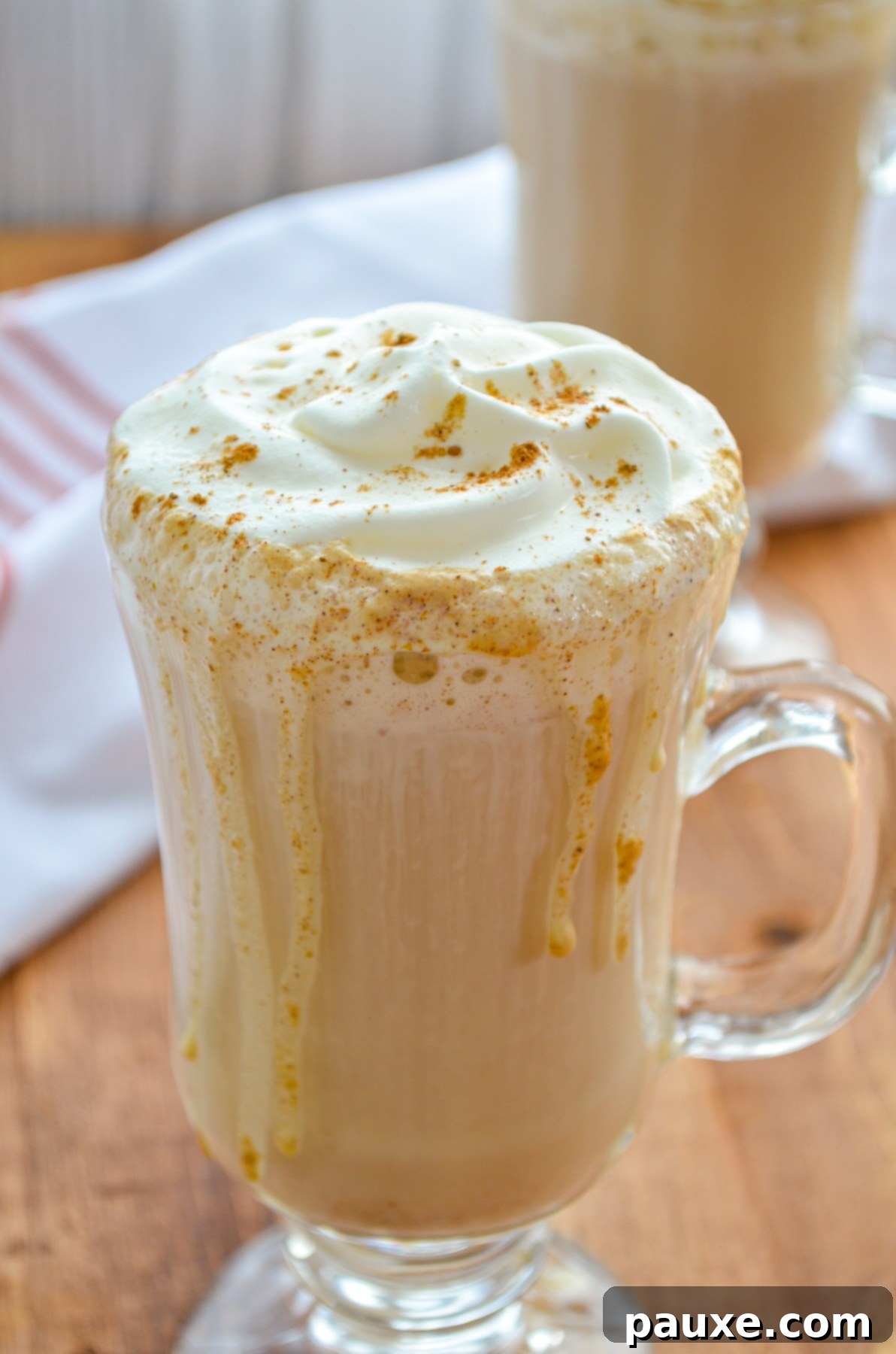 Homemade Instant Pot Pumpkin Spice Latte 7 Two cozy glass mugs of pumpkin spice latte, generously topped with whipped cream and a dusting of spice, placed on a rustic wooden surface, embodying the warmth of autumn and perfect for sharing.