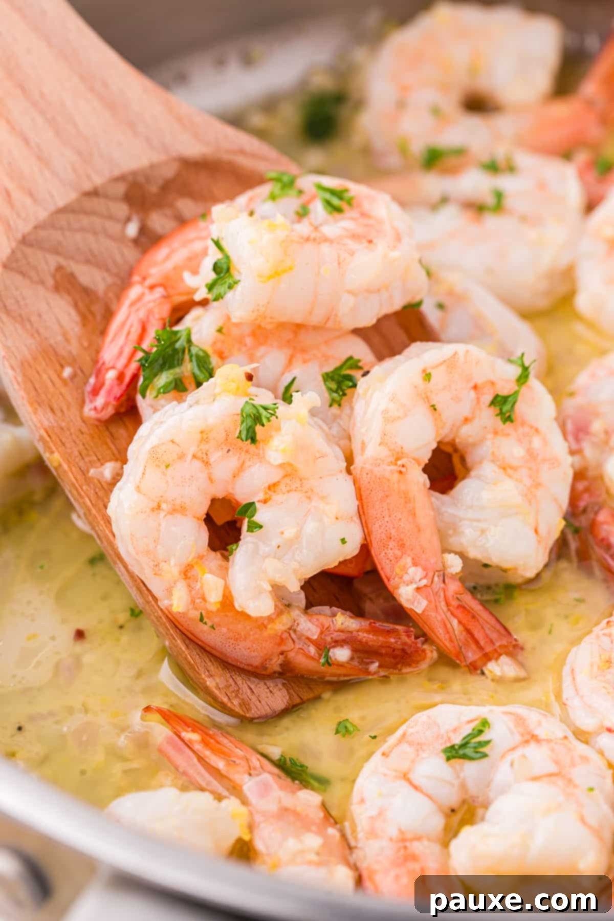 Zesty Lemon-Garlic Butter Shrimp 7 A close-up shot of a wooden spoon scooping glistening, cooked shrimp from a skillet, showing the rich garlic butter sauce.