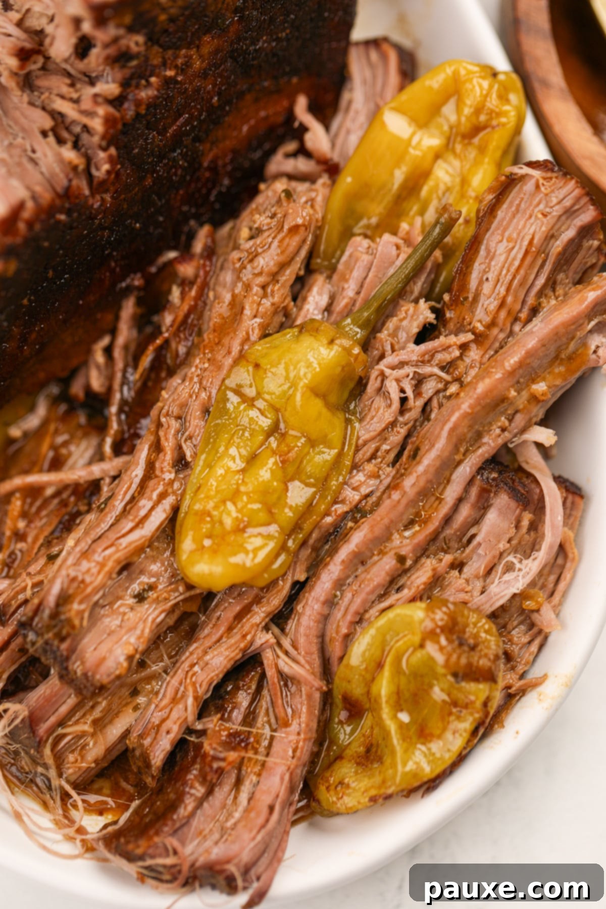 Shredded pot roast with cooked pepperoncini peppers alongside it, glistening with savory juices.