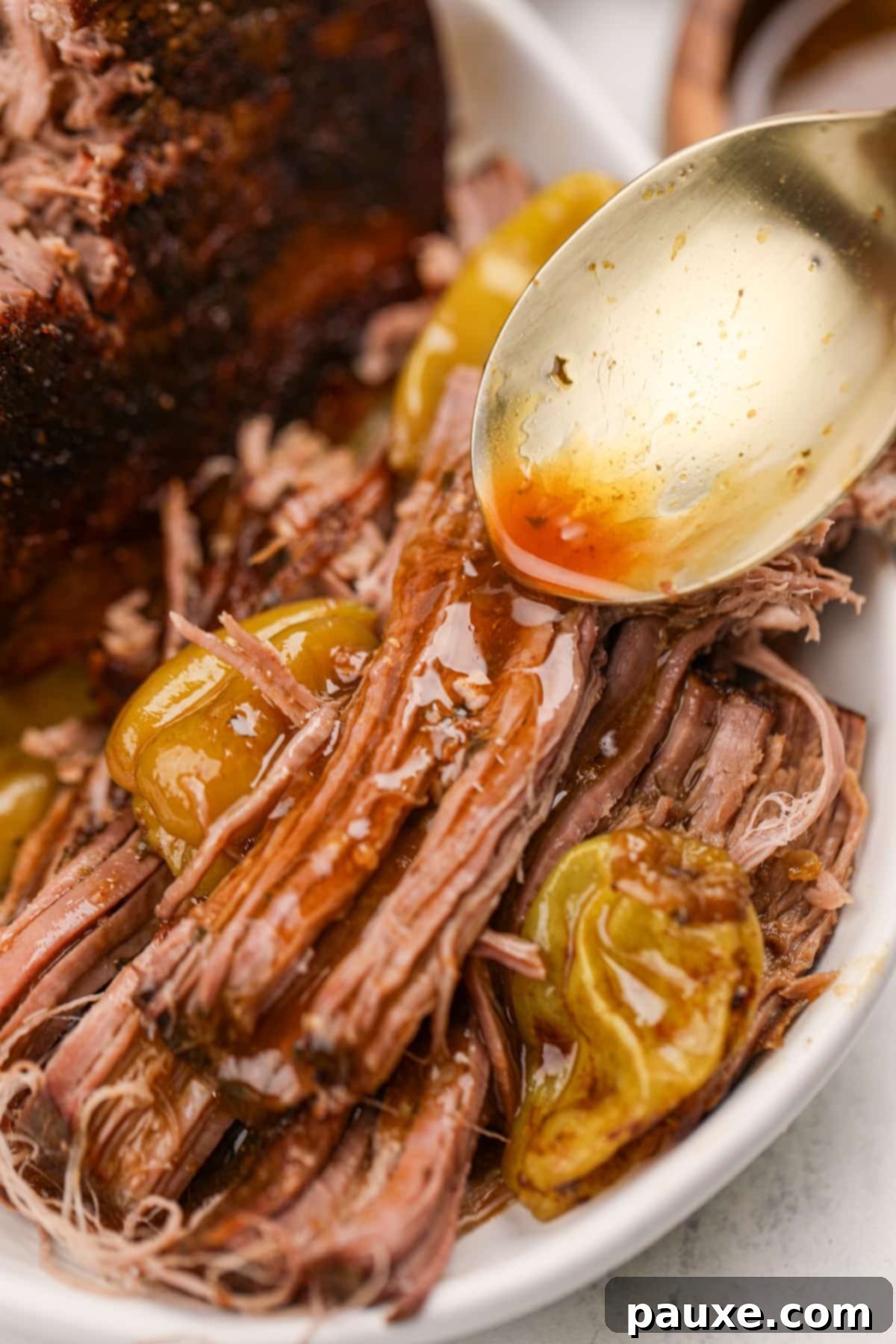 Spooning reserved juices over shredded pot roast, making it extra moist and flavorful.