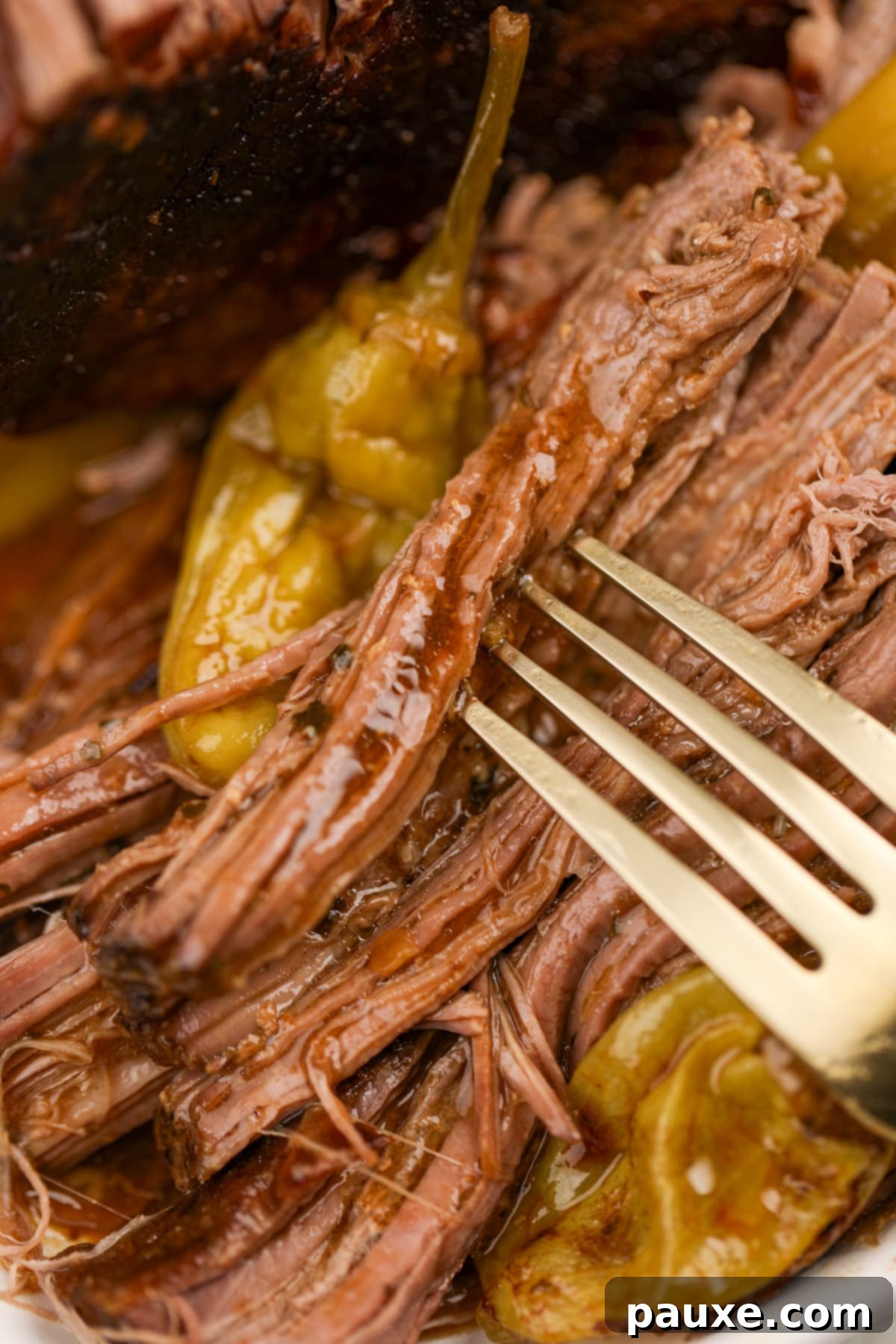 A fork taking a piece of pot roast; a pepperoncini pepper in the background.