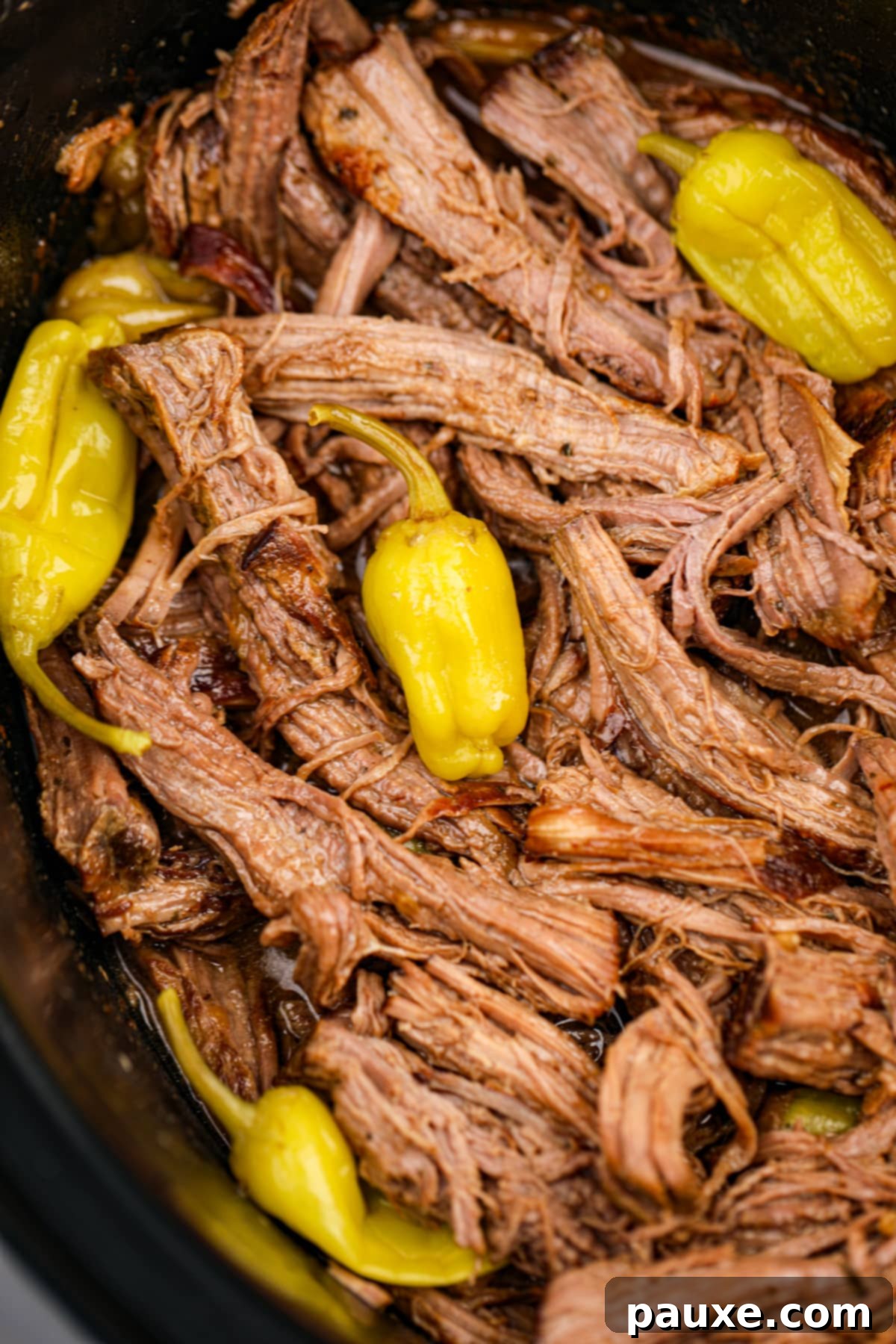 Shredded pot roast in a slow cooker, garnished with mini peppers.