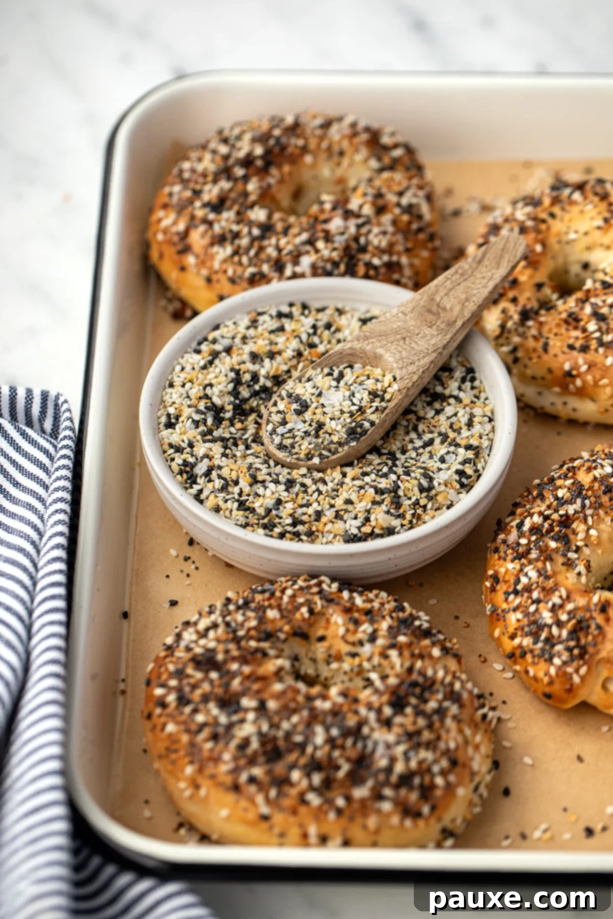 The Ultimate Seed & Spice Blend 8 A small bowl of everything bagel seasoning on a baking tray surrounded by everything bagels.