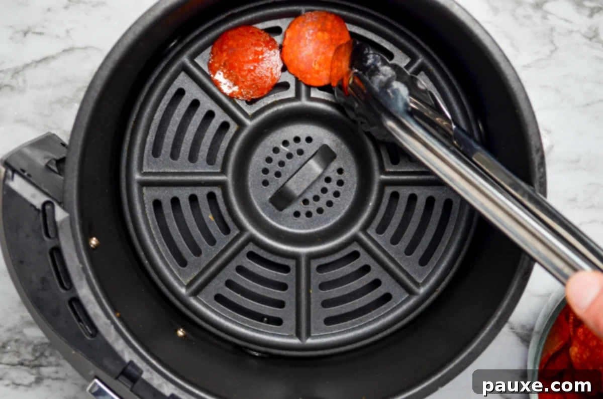 Air Fried Crispy Pepperoni 5 A set of tongs placing pepperoni slices in the basket of an air fryer.