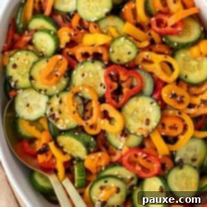 A bowl of sliced cucumber and sliced mini pepper tossed with dressing and a sprinkling of sesame seeds.