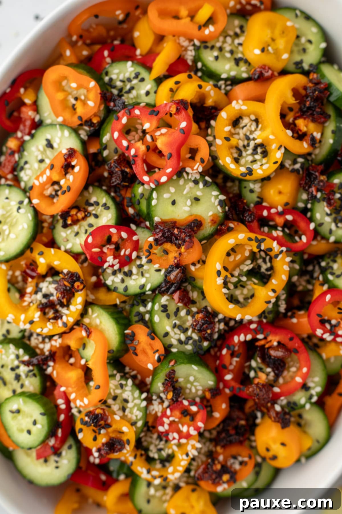 A large bowl filled with cucumber and bell pepper slices, and topped with sesame seeds and chili crisp.