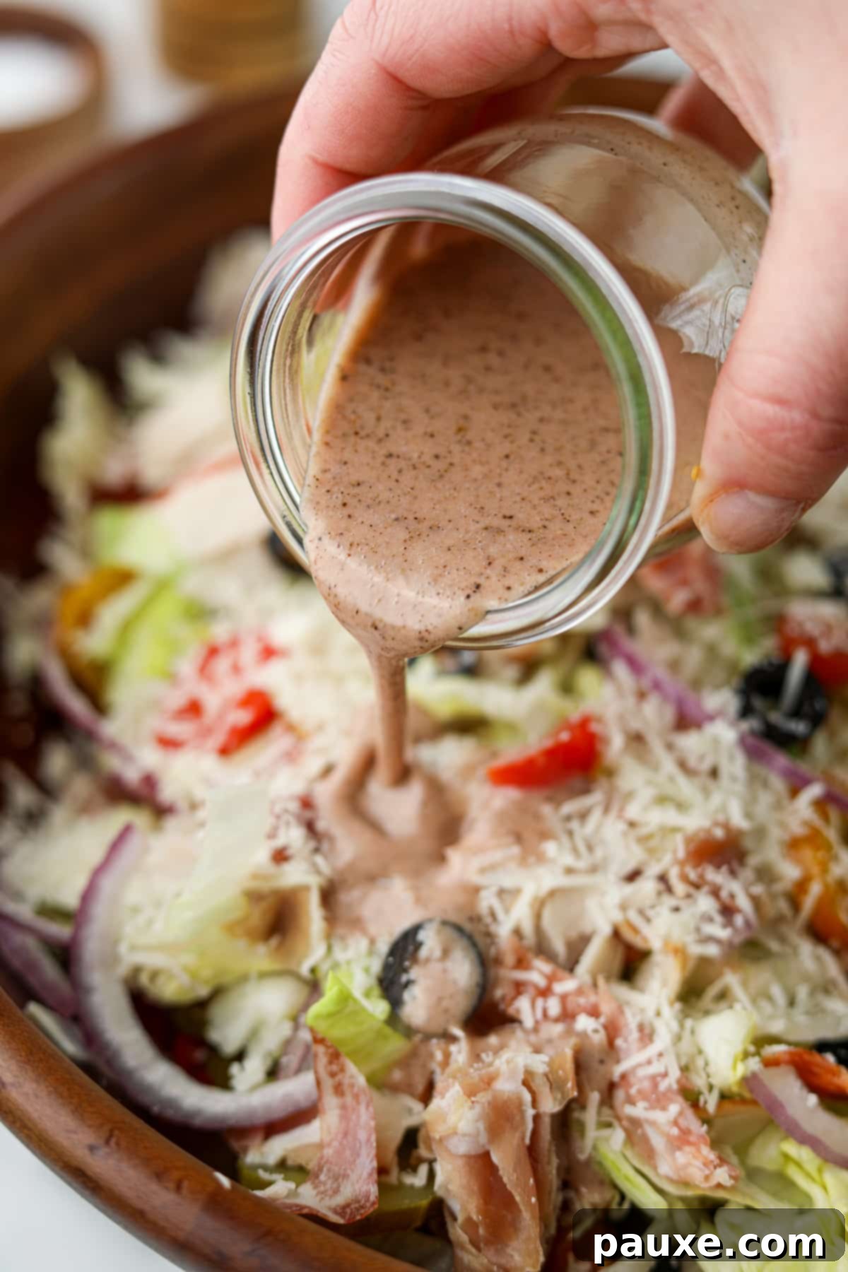 The Sub Secret 7 Drizzling sub sauce on top of a chopped salad with red onion, tomato, and lettuce, showcasing its perfect consistency.