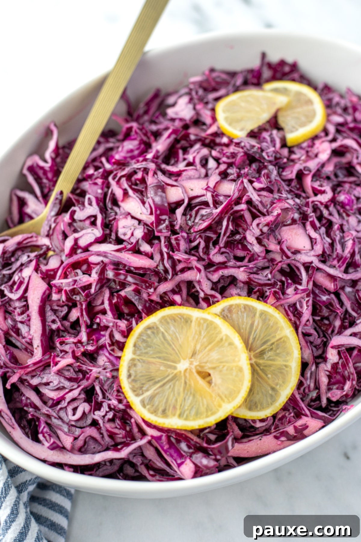 Fresh Israeli Cabbage Slaw 11 A spoon resting along the side of an elegant oval bowl of vibrant red cabbage salad, ready to be served or enjoyed.