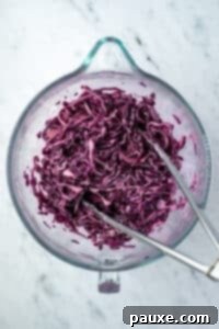 Fresh Israeli Cabbage Slaw 15 The creamy dressing being poured over the red cabbage in a large bowl, ready for tossing.
