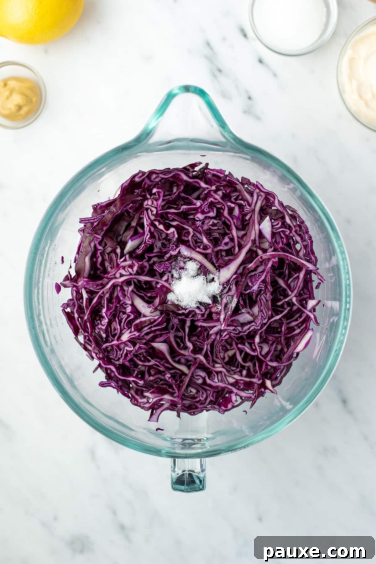 Fresh Israeli Cabbage Slaw 5 A large glass bowl filled with finely shredded red cabbage, glistening slightly after being salted.
