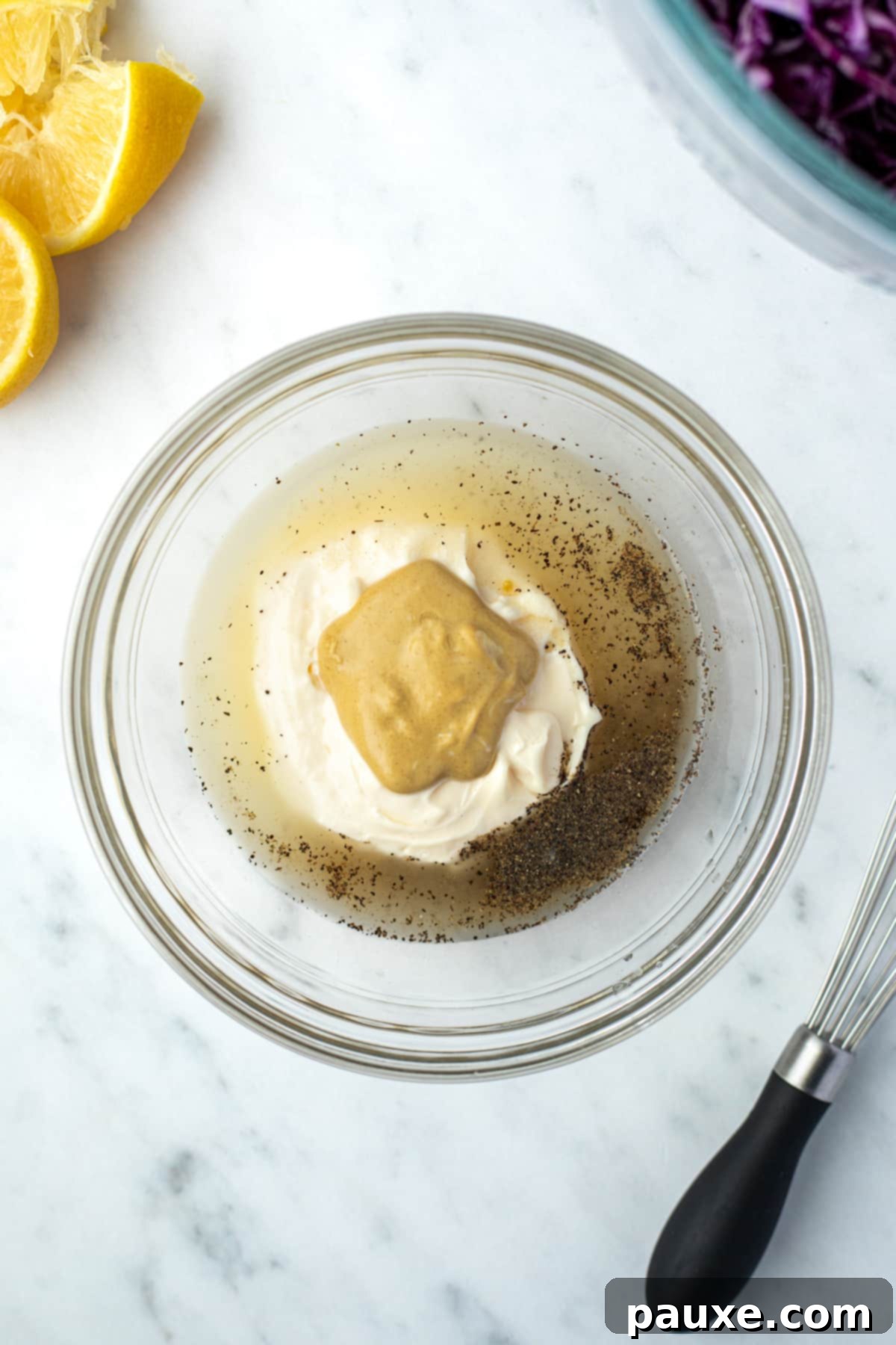 Fresh Israeli Cabbage Slaw 6 An overhead view of a small bowl containing fresh lemon juice, creamy mayonnaise, tangy Dijon mustard, and a sprinkle of black pepper, ready to be whisked into a dressing.