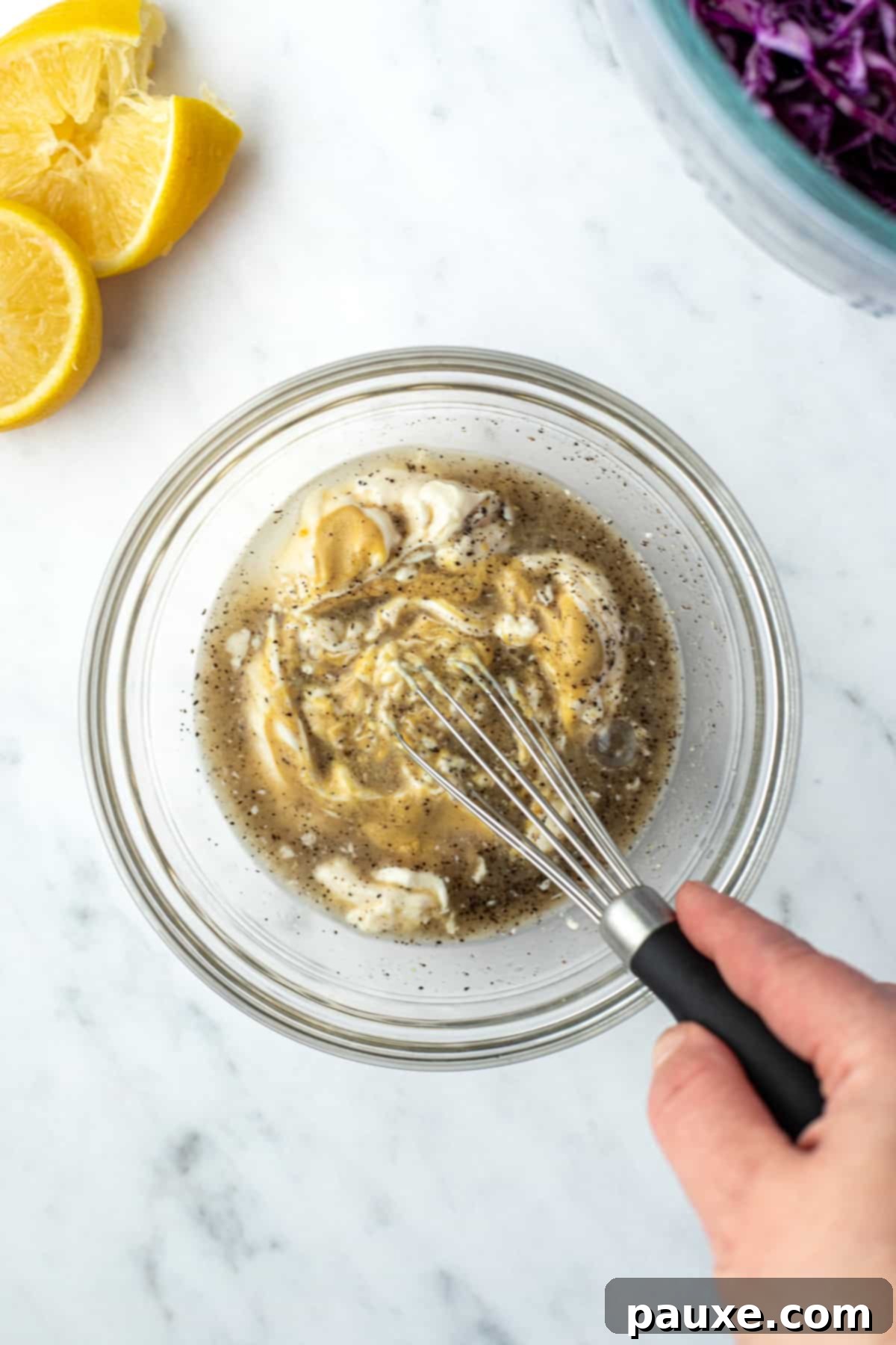 Fresh Israeli Cabbage Slaw 7 A hand whisking together mayonnaise, lemon juice, Dijon mustard, and black pepper in a bowl, creating a smooth and emulsified dressing.