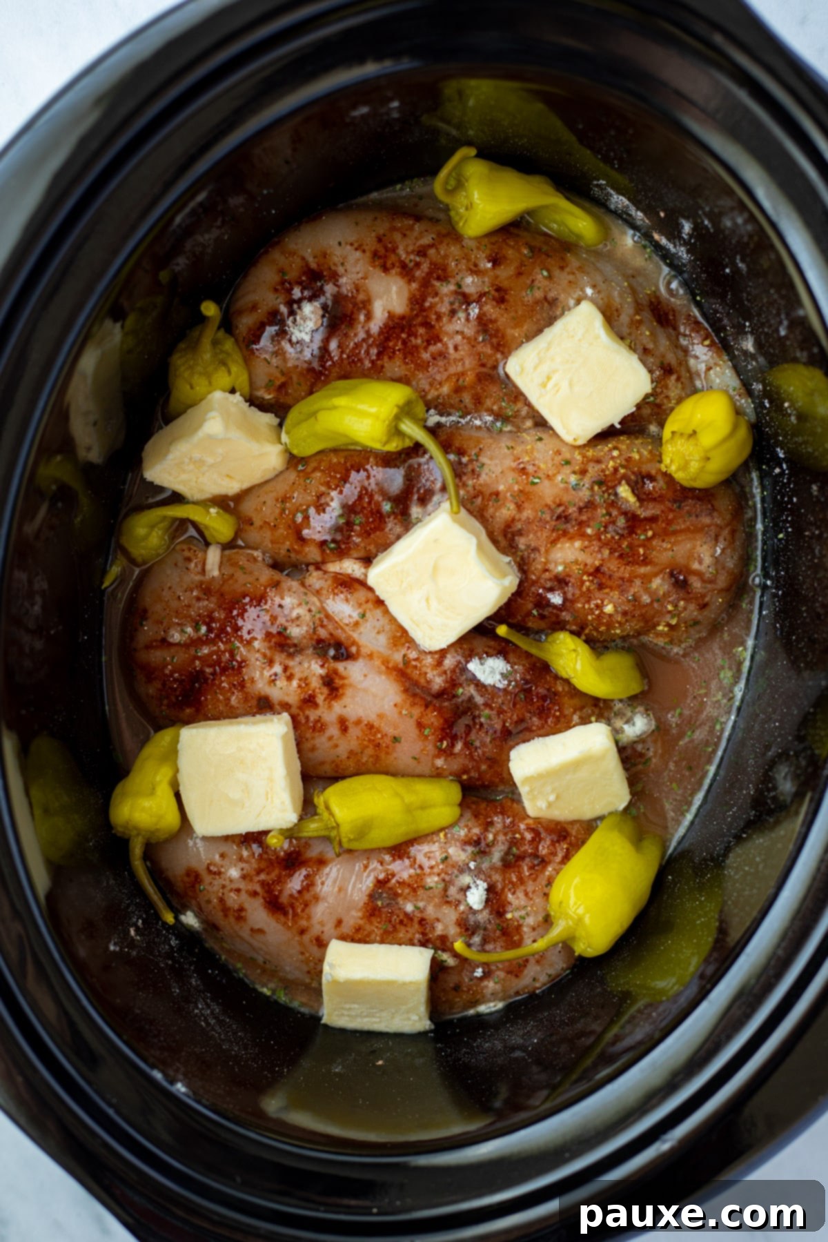 Mississippi Pot Roast Chicken 5 A slow cooker filled with chicken, seasonings, chicken broth, pepperoncini peppers, and butter slices.