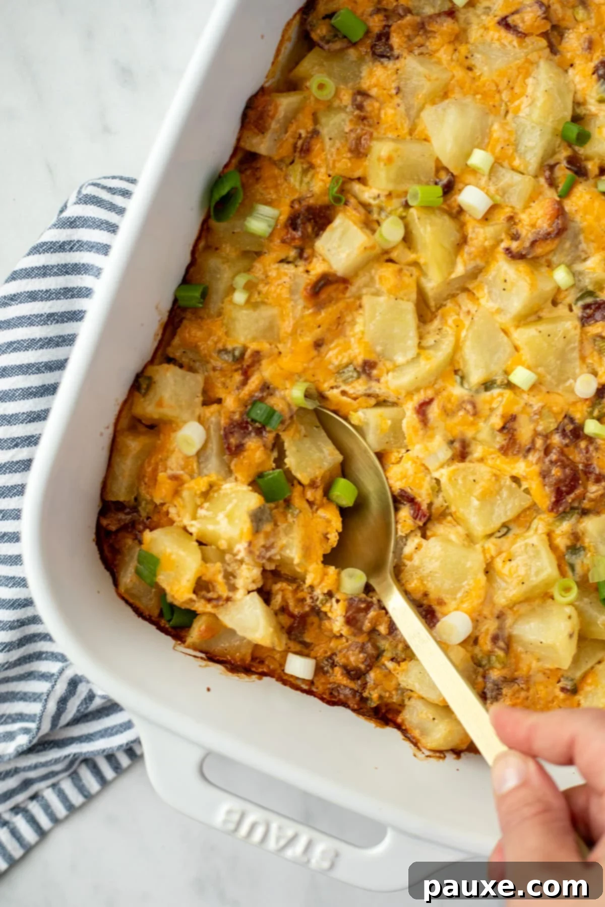 Deep South Midnight Spuds 7 A spoon taking a portion of potatoes from a white baking dish.