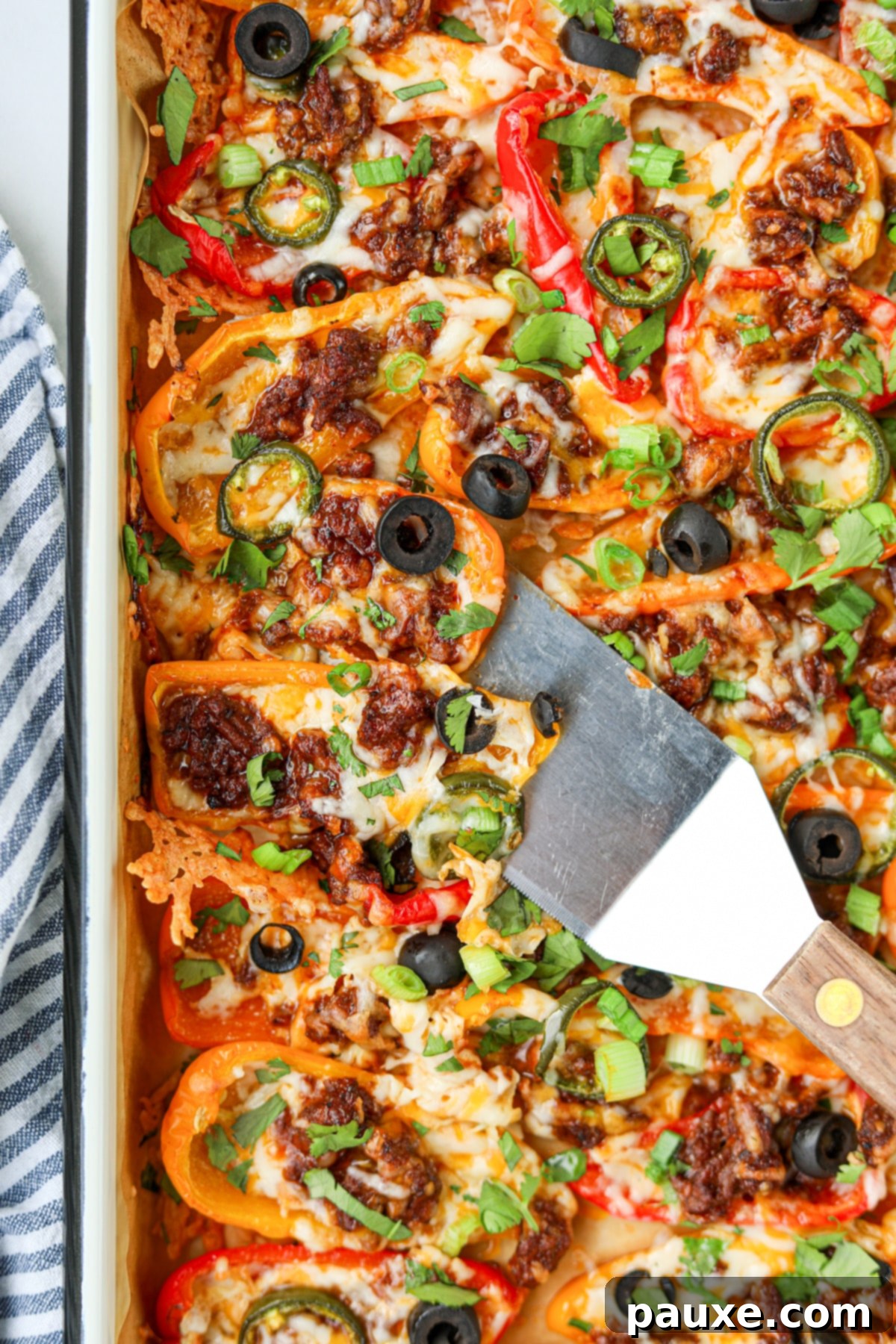 Bell Pepper Nacho Boats 2 A sheet pan generously laden with colorful bell pepper nachos, featuring vibrant melted cheese, seasoned ground beef, and fresh, zesty toppings. A small spatula is carefully lifting a portion from the pan, highlighting the delicious layers.