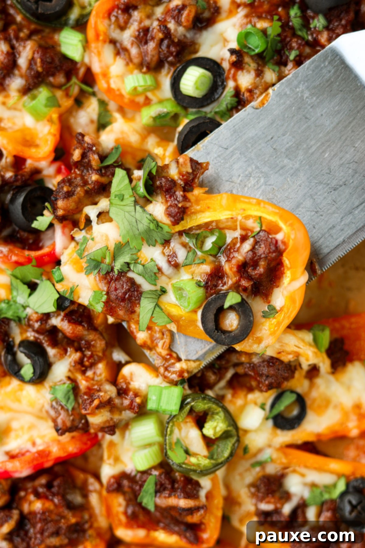 Bell Pepper Nacho Boats 6 A perfectly assembled mini bell pepper nacho, with richly melted cheese, seasoned meat, and a bright slice of jalapeno, being delicately lifted from a baking sheet by hand.