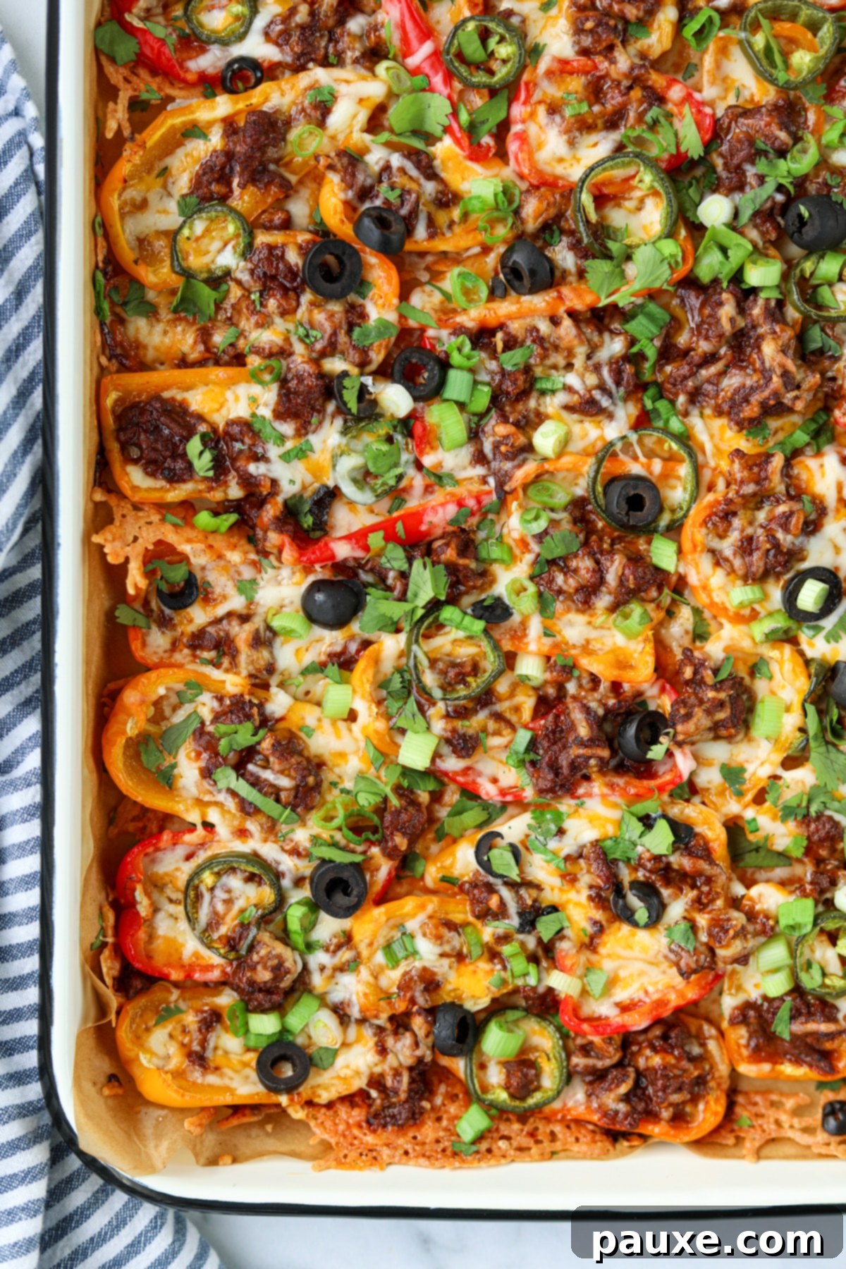 Bell Pepper Nacho Boats 7 A stunning close-up of a pan brimming with beautifully baked mini pepper nachos, featuring golden melted cheese, scattered black olives, vibrant sliced jalapenos, and a hint of fresh green onions, ready to be served.