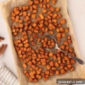 Golden Roasted Sweet Potato Bites 12 A sheet pan filled with golden roasted sweet potato cubes, with a serving spoon taking a portion.
