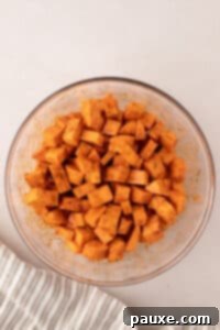 Golden Roasted Sweet Potato Bites 13 A bowl of uniformly cubed sweet potatoes perfectly tossed in seasonings and oil, showing an even coating.