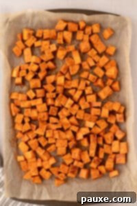 Golden Roasted Sweet Potato Bites 14 A parchment-lined baking sheet with seasoned sweet potato cubes spread in a single, uncrowded layer.