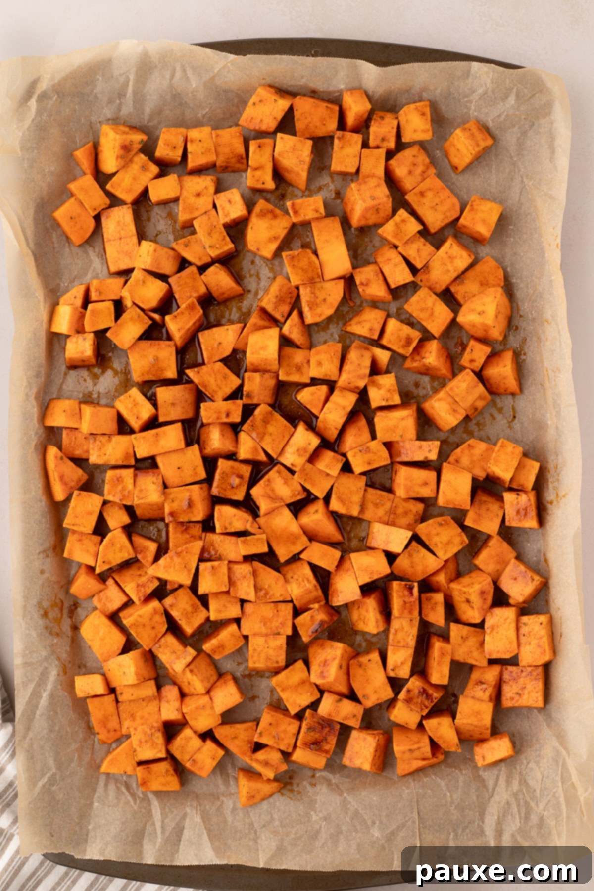 Golden Roasted Sweet Potato Bites 6 A parchment-lined baking sheet with seasoned sweet potato cubes spread in a single layer.