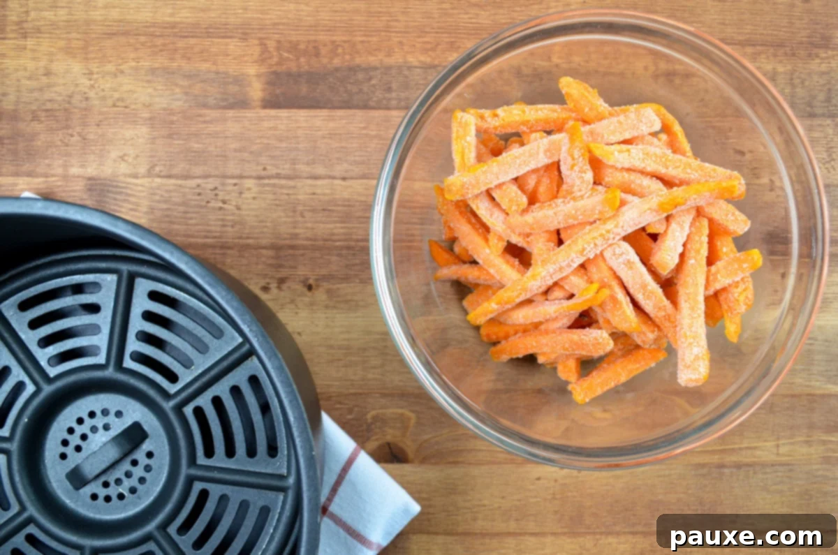 Crispy Air Fryer Sweet Potato Fries 3 A bowl of uncooked frozen sweet potato fries next to a black basket-style air fryer.