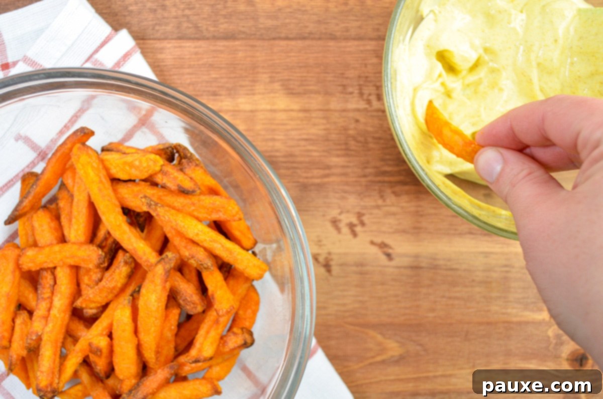 Crispy Air Fryer Sweet Potato Fries 6 A sweet potato fry being dipped into a bowl of homemade curry mayo.