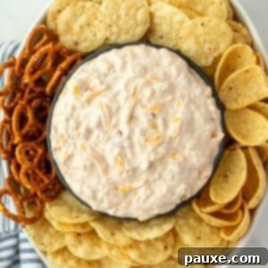 An oval dish filled with tortilla chips and other dippables, with a bowl of creamy cheese and corn dip in the center.