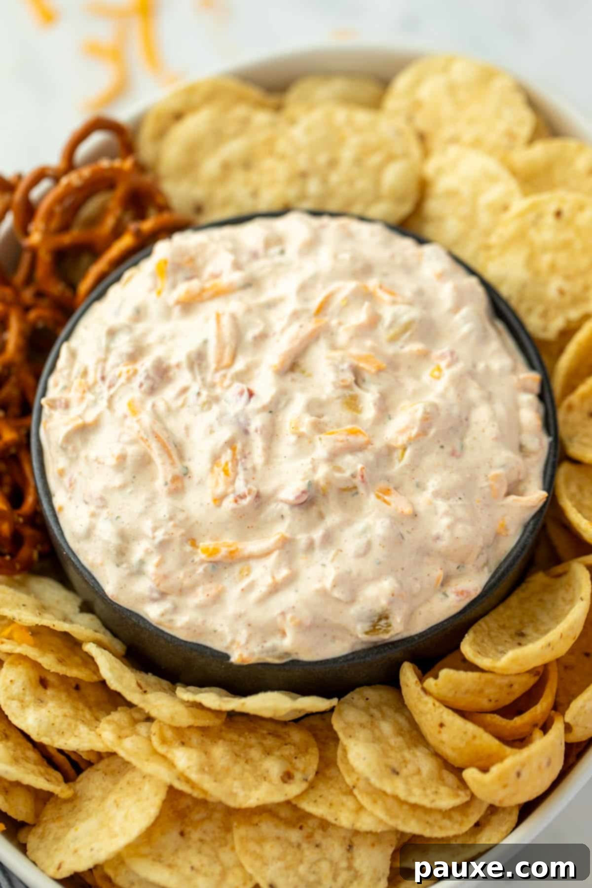 A bowl of creamy dip surrounded by tortilla chips, corn chips, pretzels, etc.