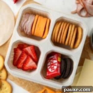 Craft-Your-Own Lunch Kits 10 A lunch container with four sections, filled with meat, cheese, crackers, fruit, and a mini chocolate bar, showcasing a delightful homemade lunchable.