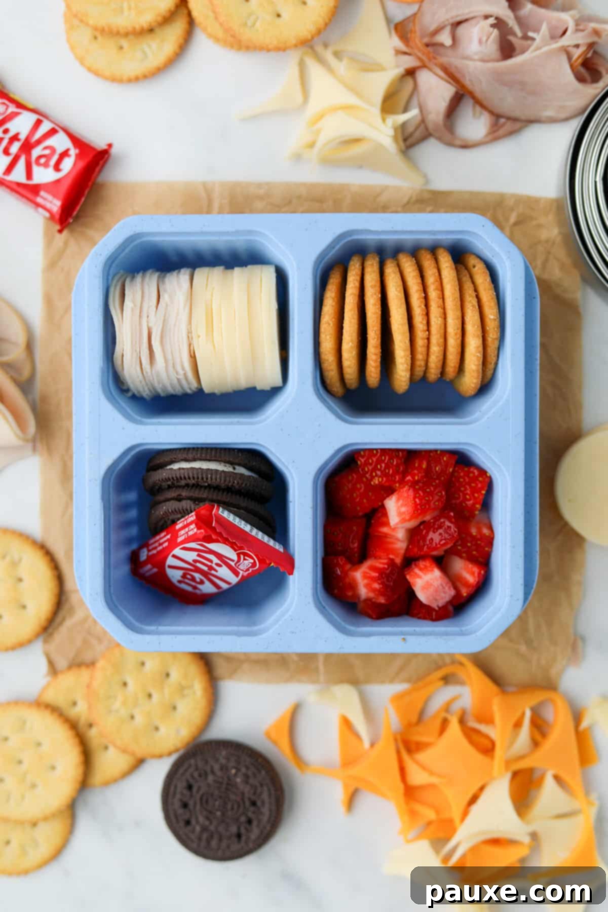 Craft-Your-Own Lunch Kits 9 A simple yet satisfying lunch container, artfully arranged with cheese rounds, crackers, fresh fruit, and a charming mini chocolate bar, perfect for a quick and enjoyable meal.