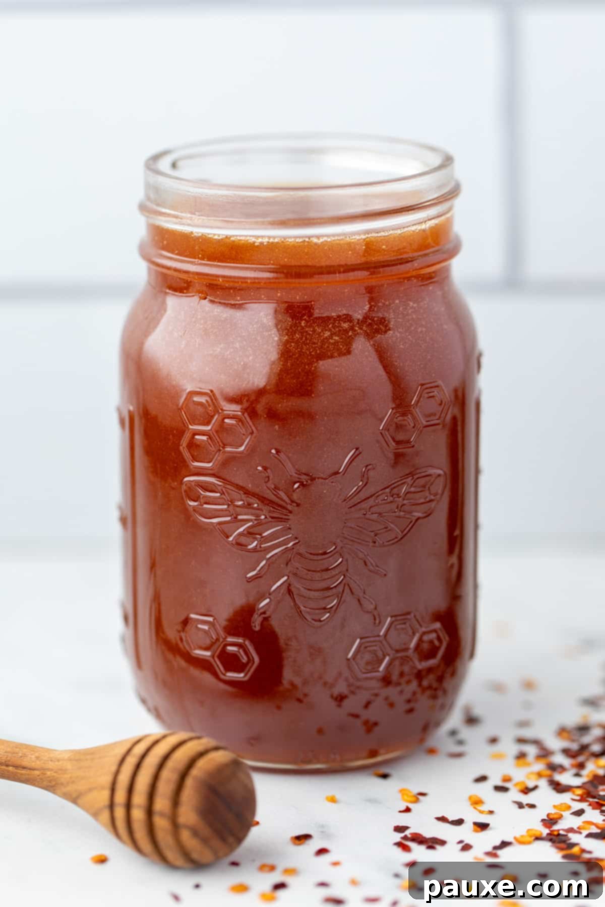 Crafting Homemade Hot Honey 2 A jar of hot honey with a honey dipper on the side and crushed chiles on the counter, symbolizing the delicious blend of sweet and spicy.