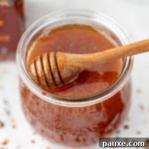 Crafting Homemade Hot Honey 11 A jar of hot honey with a loaded honey dipper, and scattered crushed red pepper flakes on the counter, ready to be enjoyed.