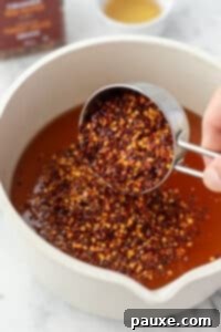 Crafting Homemade Hot Honey 13 Adding dried red pepper flakes to a saucepan with honey.