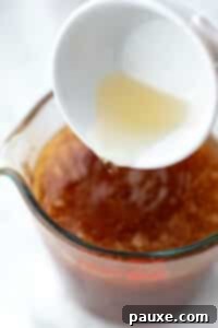 Crafting Homemade Hot Honey 15 Pouring apple cider vinegar into a measuring cup full of honey.