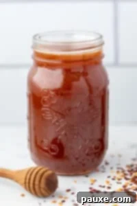 Crafting Homemade Hot Honey 16 A jar of hot honey with a honey dipper on the side and crushed chiles on the counter.
