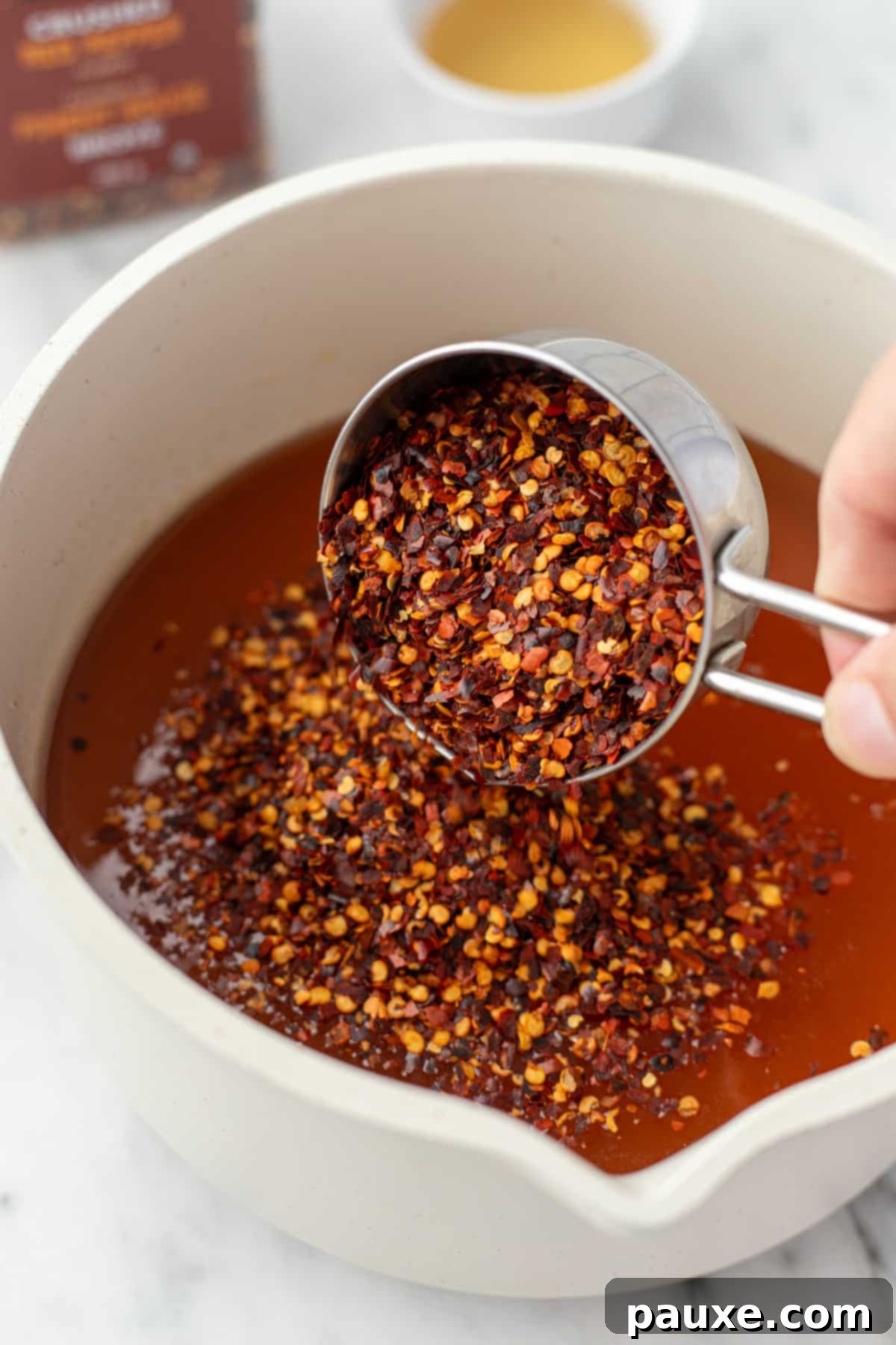 Crafting Homemade Hot Honey 5 Adding dried red pepper flakes to a saucepan with warm honey, initiating the infusion process.