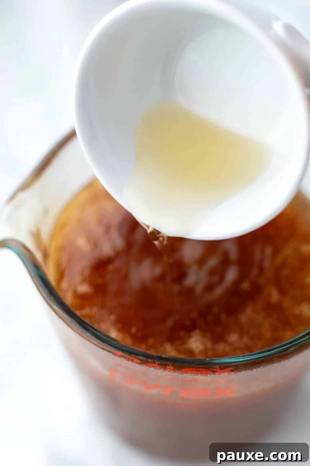 Crafting Homemade Hot Honey 7 Pouring apple cider vinegar into a measuring cup full of strained hot honey, adding the final touch.